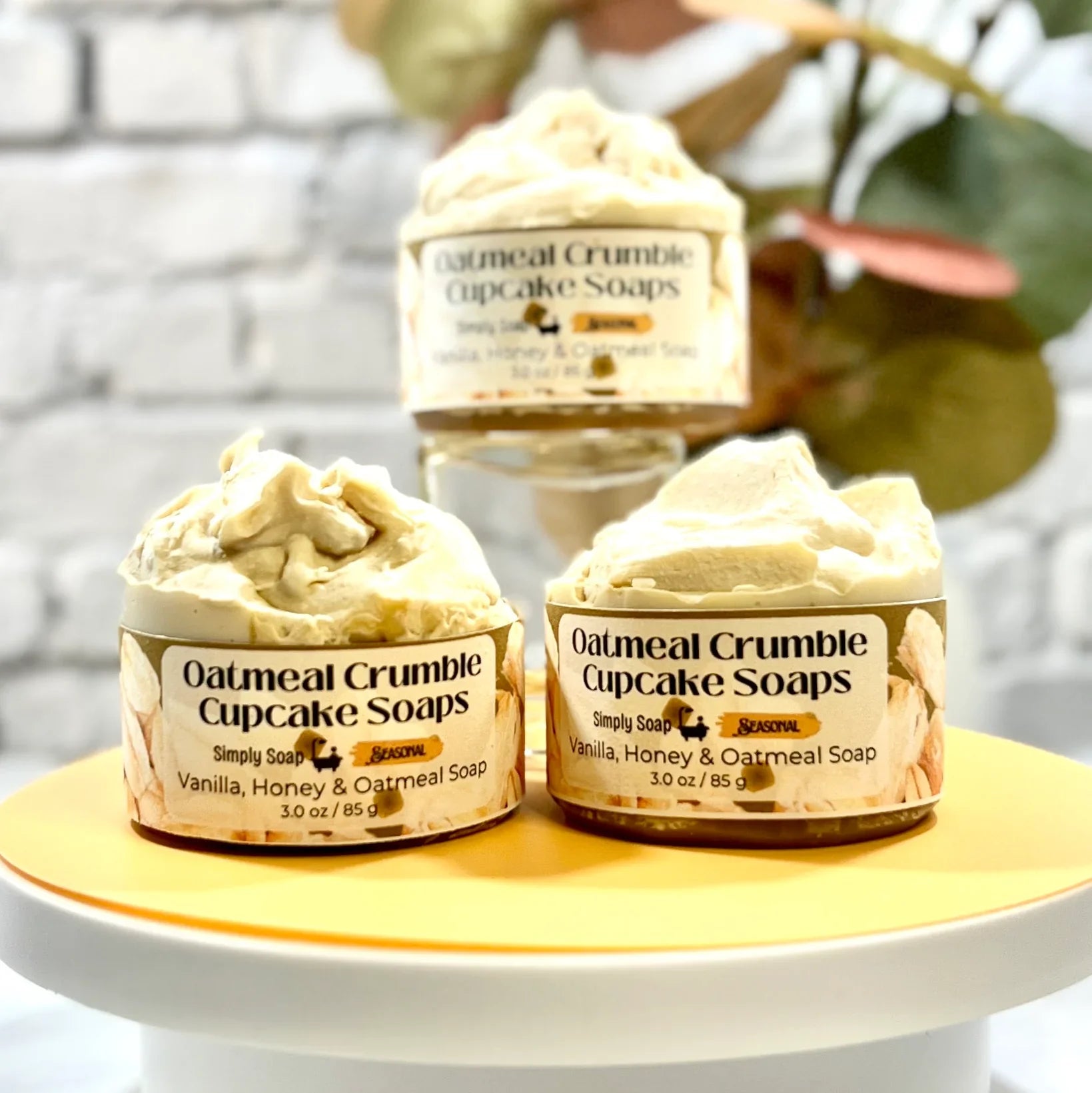 Three Oatmeal Crumble Cupcake Soaps on a white stand with a blurred background