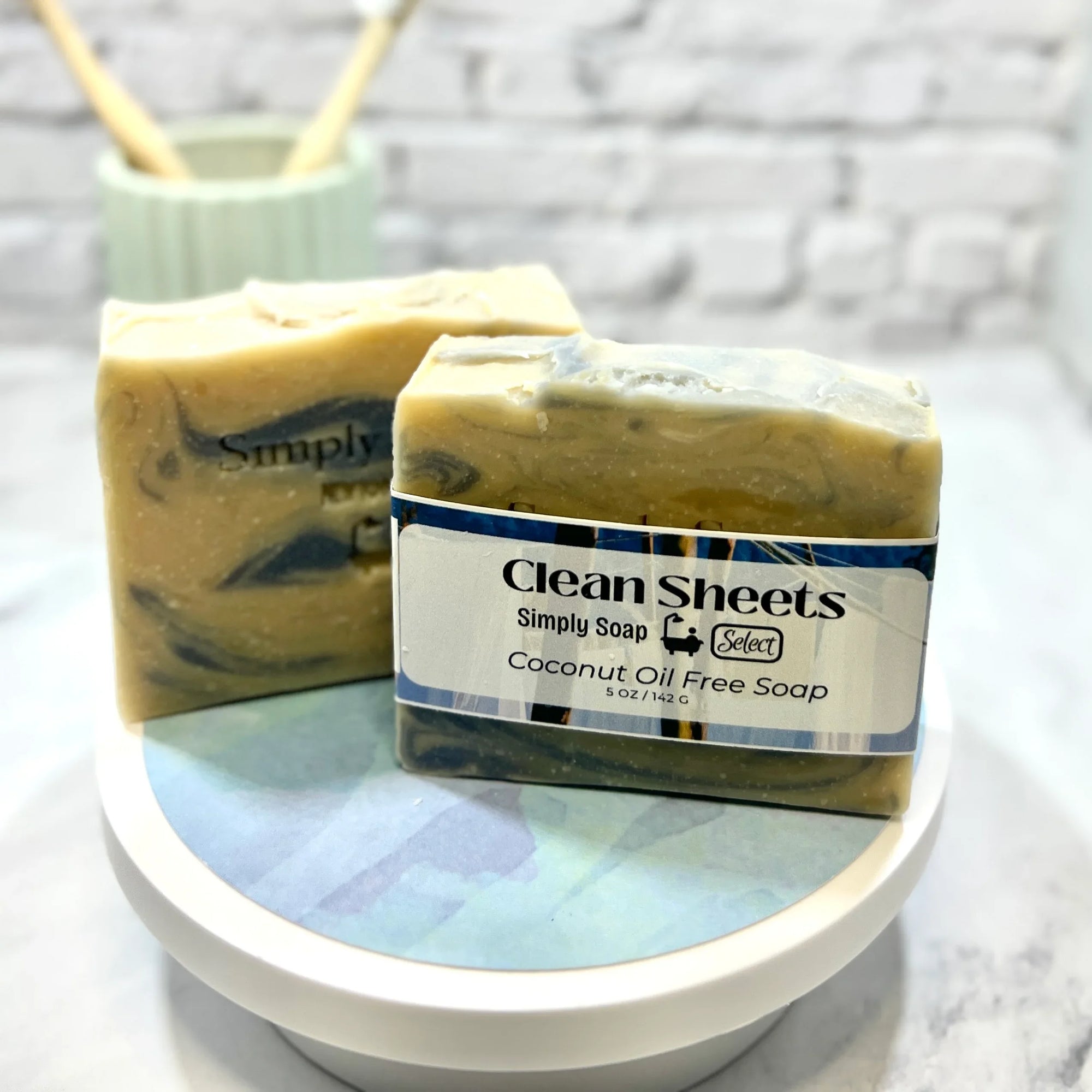 Two bars of soap, one labeled 'Clean Sheets' and the other 'Simply Soap', on a white surface with a blurred background.