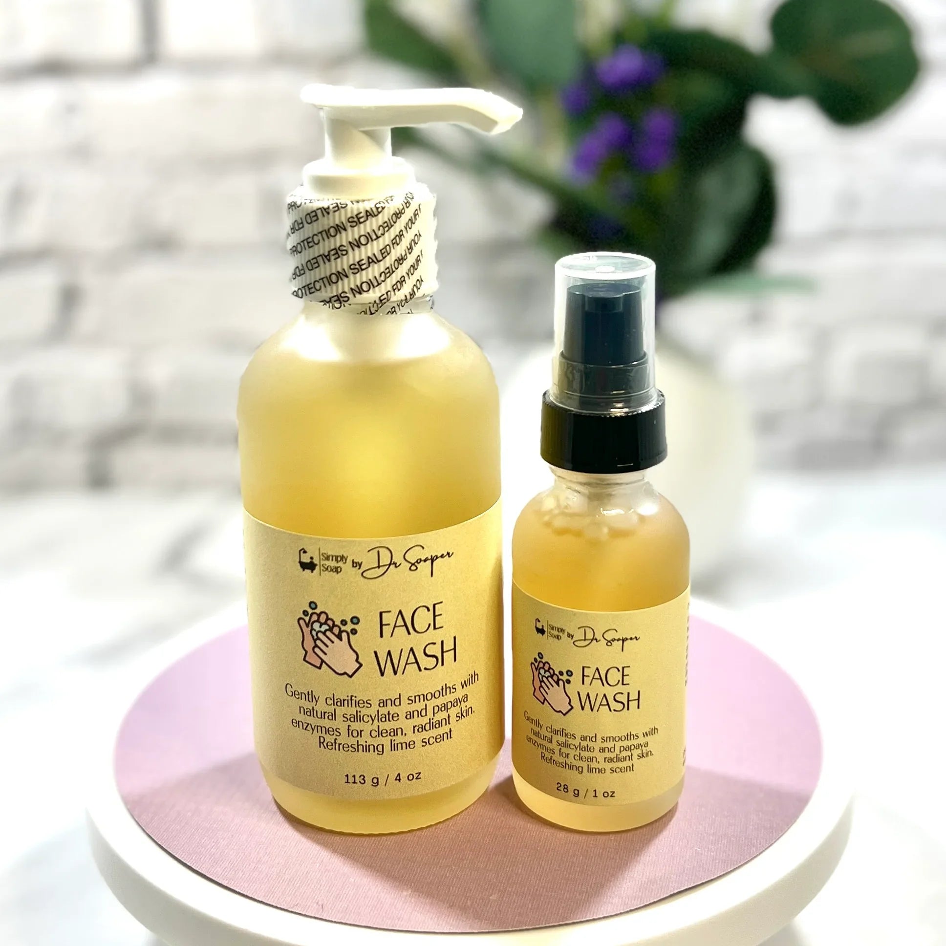 Two bottles of face wash, one large and one small, on a pink and white circular stand with a blurred background.