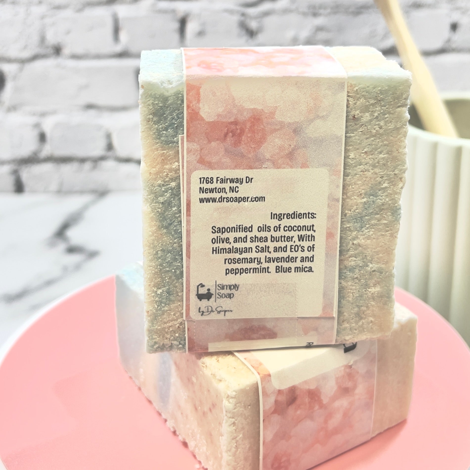 Bar of soap with back label on a pink stand against a brick  background