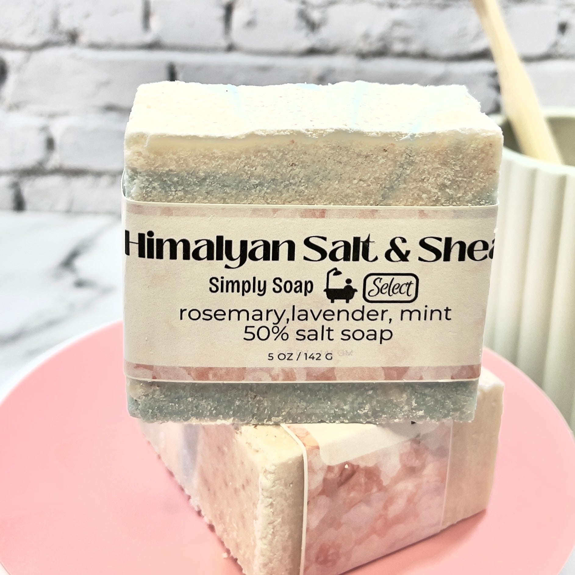 Bar of soap with a label on a pink stand against a gray brick wall.