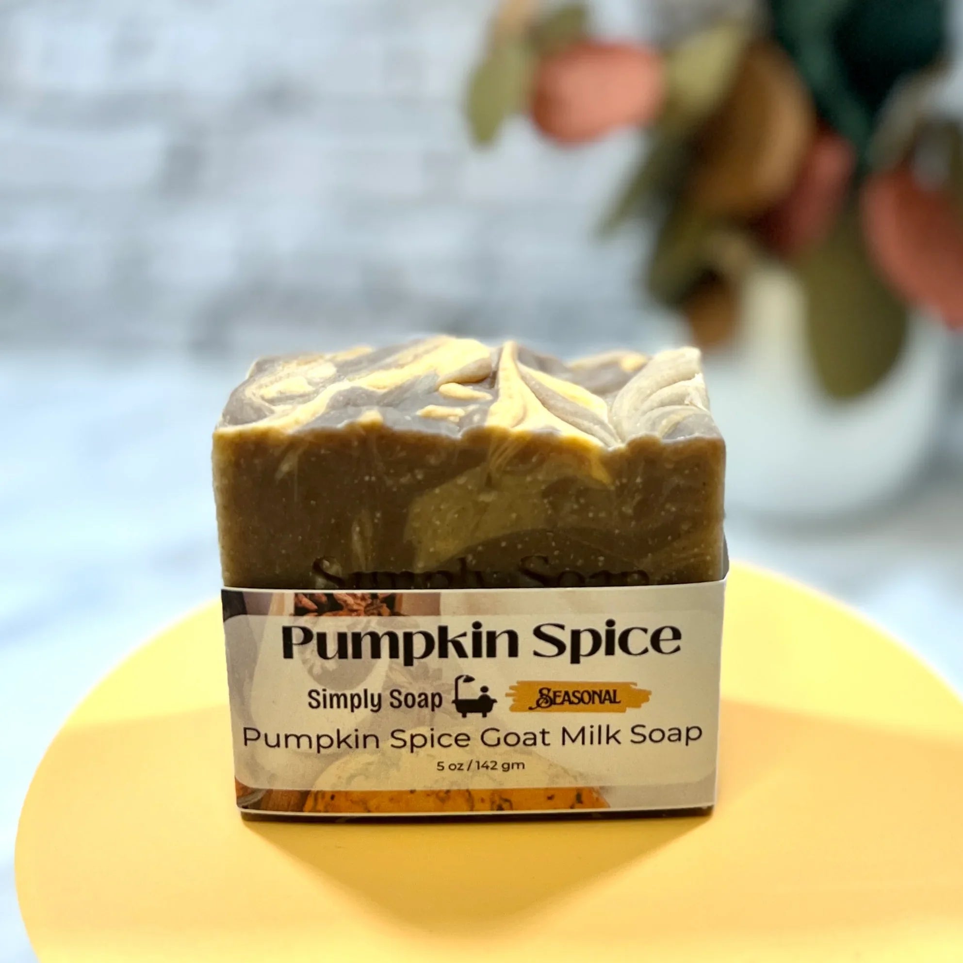 Bar of pumpkin spice goat milk soap on a yellow plate with a blurred background