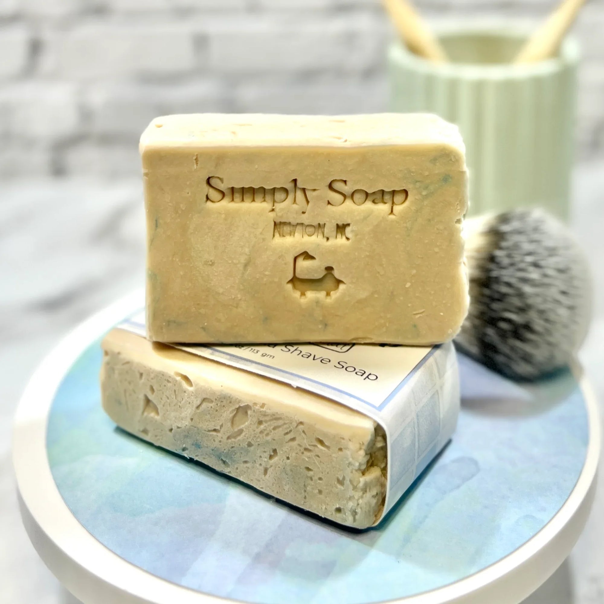 Two bars of 'Simply Soap' on a round white plate with a blurred background