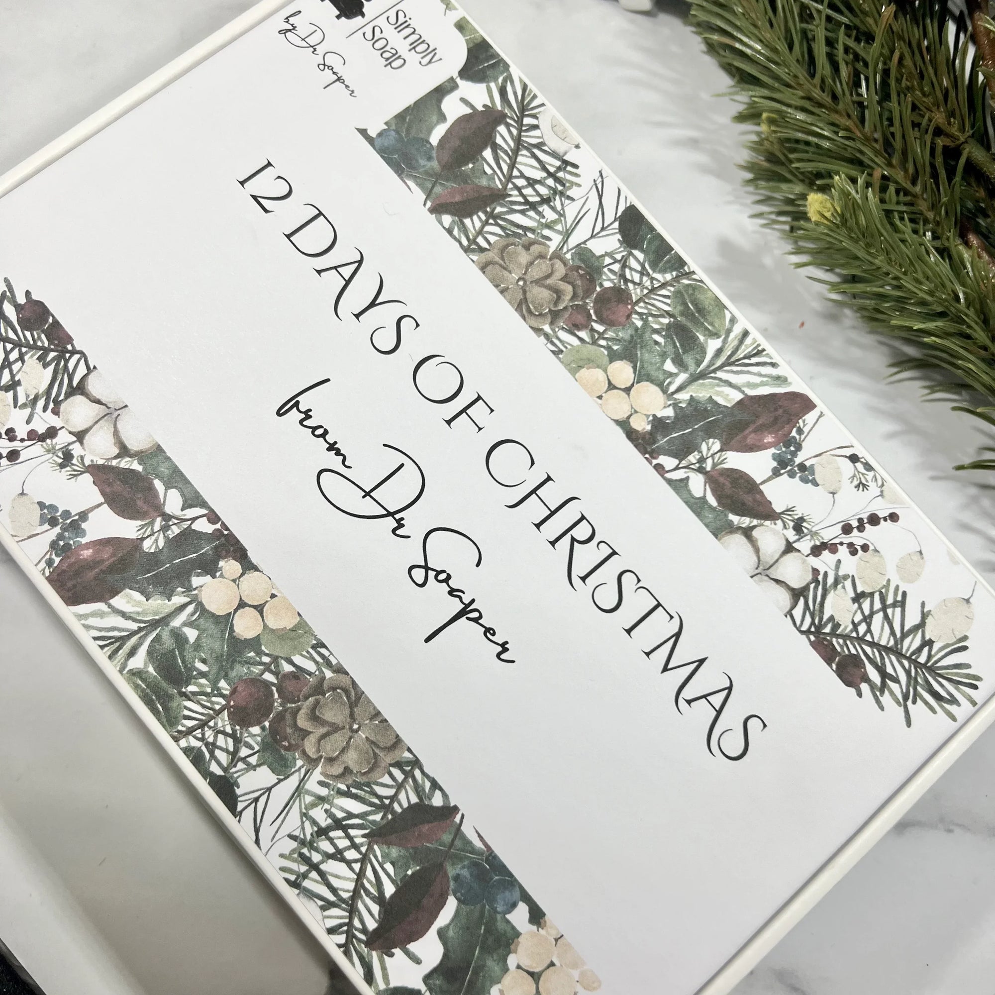 A decorative box labeled '12 DAYS OF CHRISTMAS FROM DR. SOAPER' with a floral and pine needle design.