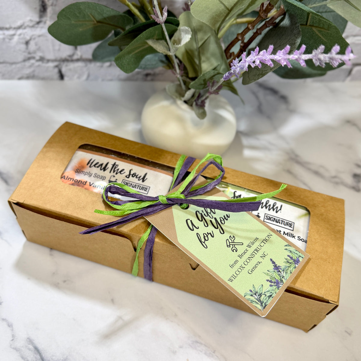 A kraft paper gift box containing two bars of soap, tied with a purple and green ribbon and a light green tag that reads 'A Gift for You.' 