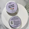 Two round metal tins of Dr Soaper's Solid Make-Up Brush Cleaner, one showing the lavender lid with product name and the other showing the back with instructions and ingredients, set on a white ceramic dish.