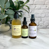 Three facial skincare products on a marble surface with a plant and brick wall in the background.