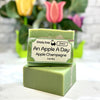 Green soap bar with 'Simply Soap Limited' label on a white surface with blurred flowers in the background