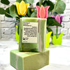 Green soap bar with a label on a white surface, surrounded by decorative tulip-shaped soaps.