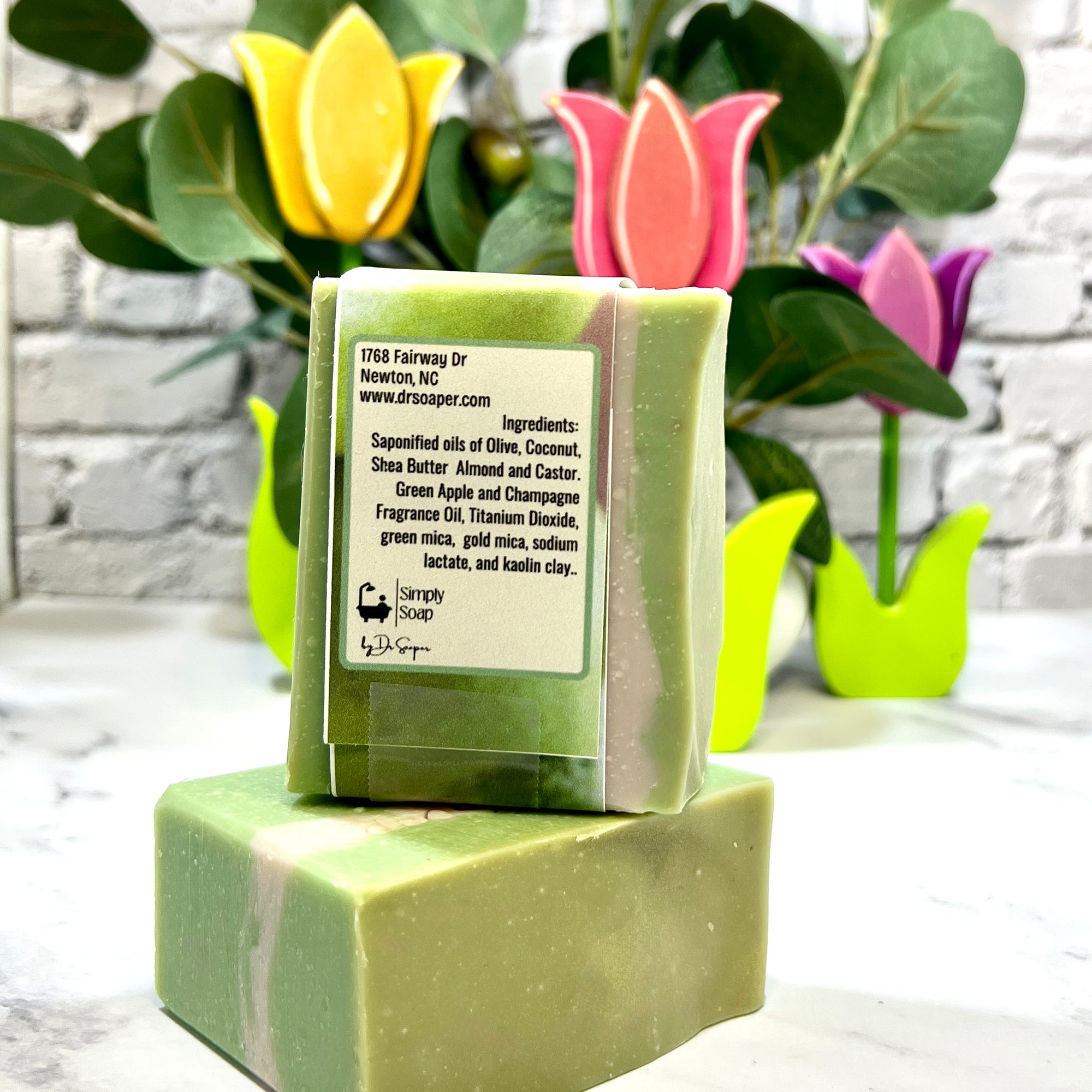 Green soap bar with a label on a white surface, surrounded by decorative tulip-shaped soaps.