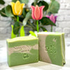 Two bars of soap with 'Simply Soap' branding in front of colorful tulips.
