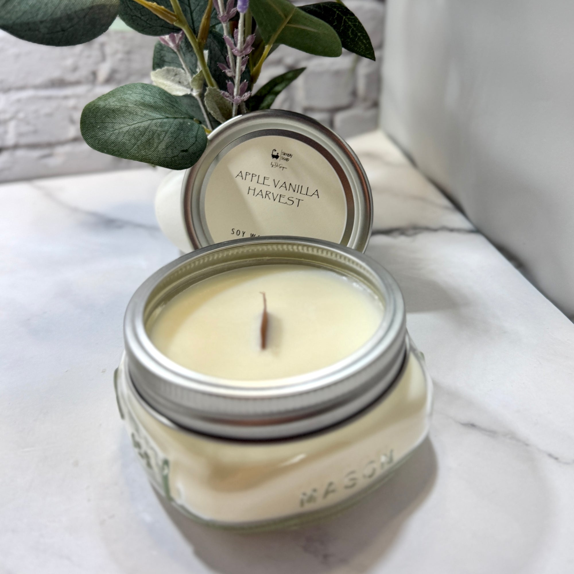 Apple vanilla harvest candle in a mason jar with a plant in the background
