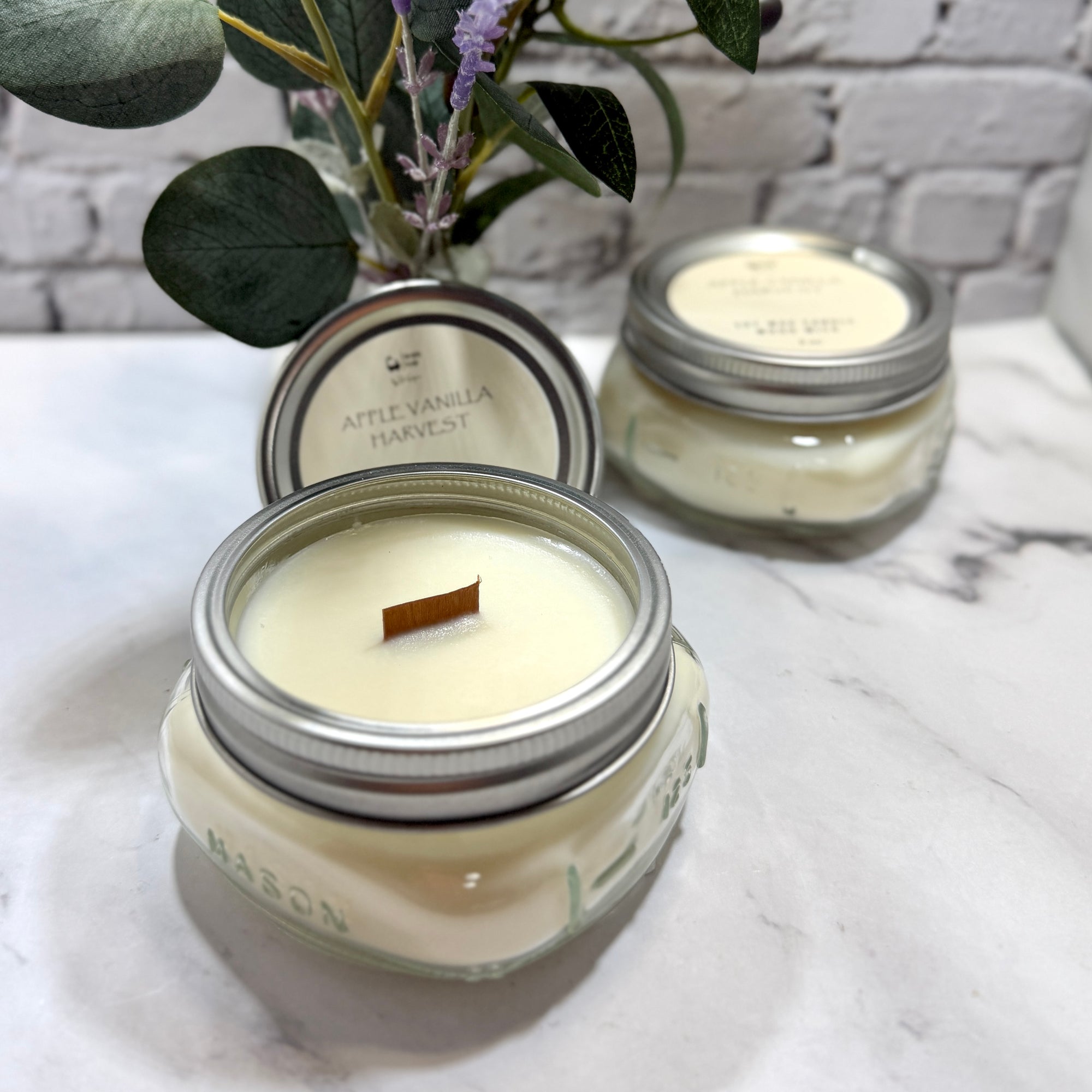 Two mason jars containing apple vanilla soy candles with wood wicks