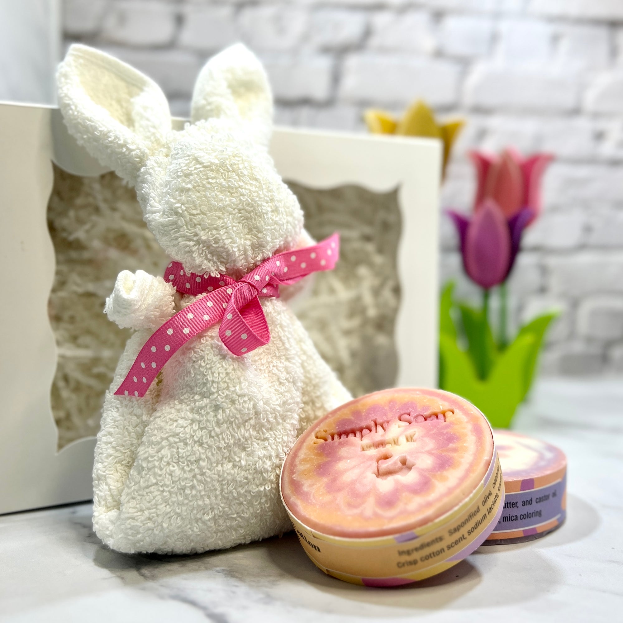 White plush bunny with a pink bow next to a jar of 'Simply Soap' on a marble surface.