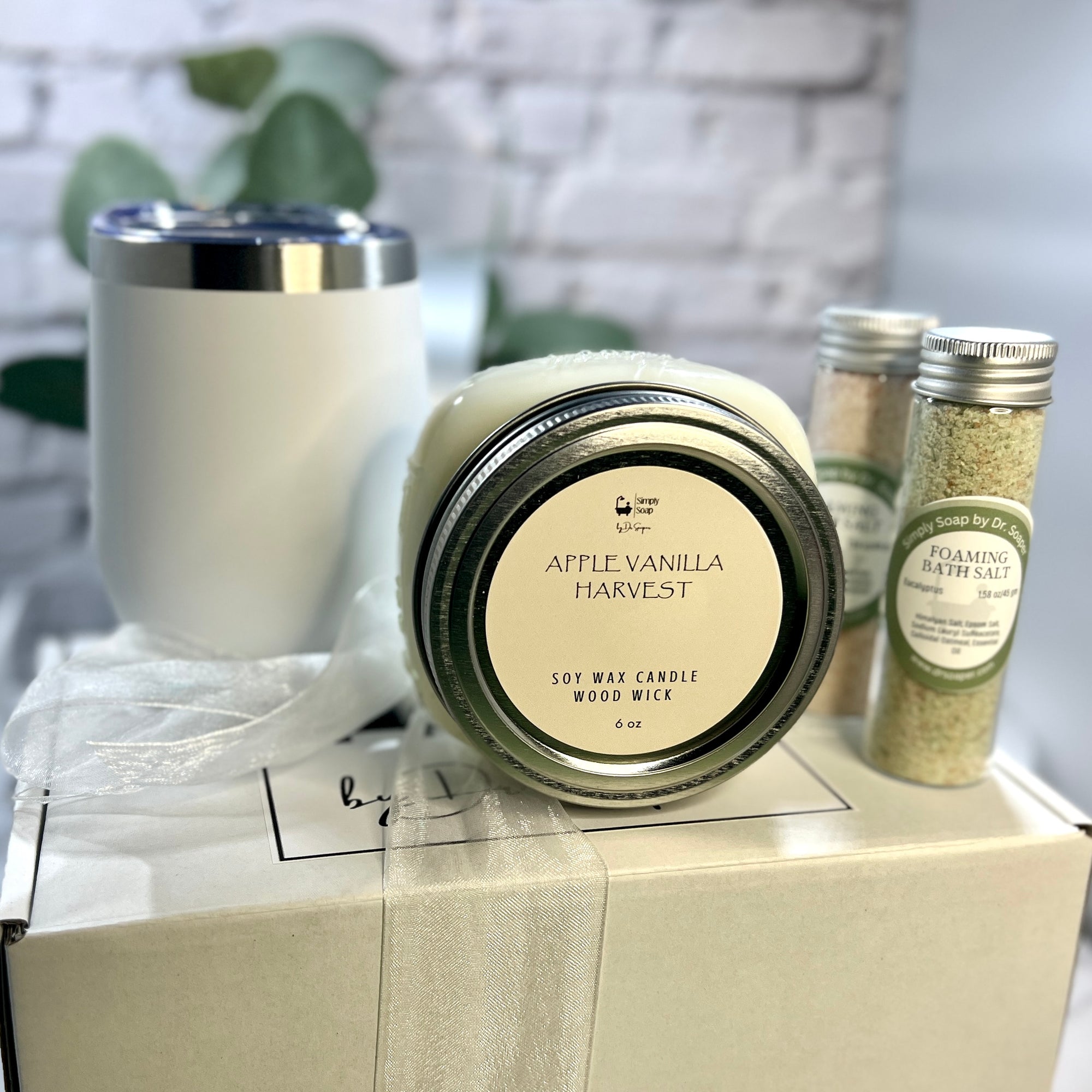 Candle labeled 'Apple Vanilla Harvest' on a box with other products in the background.