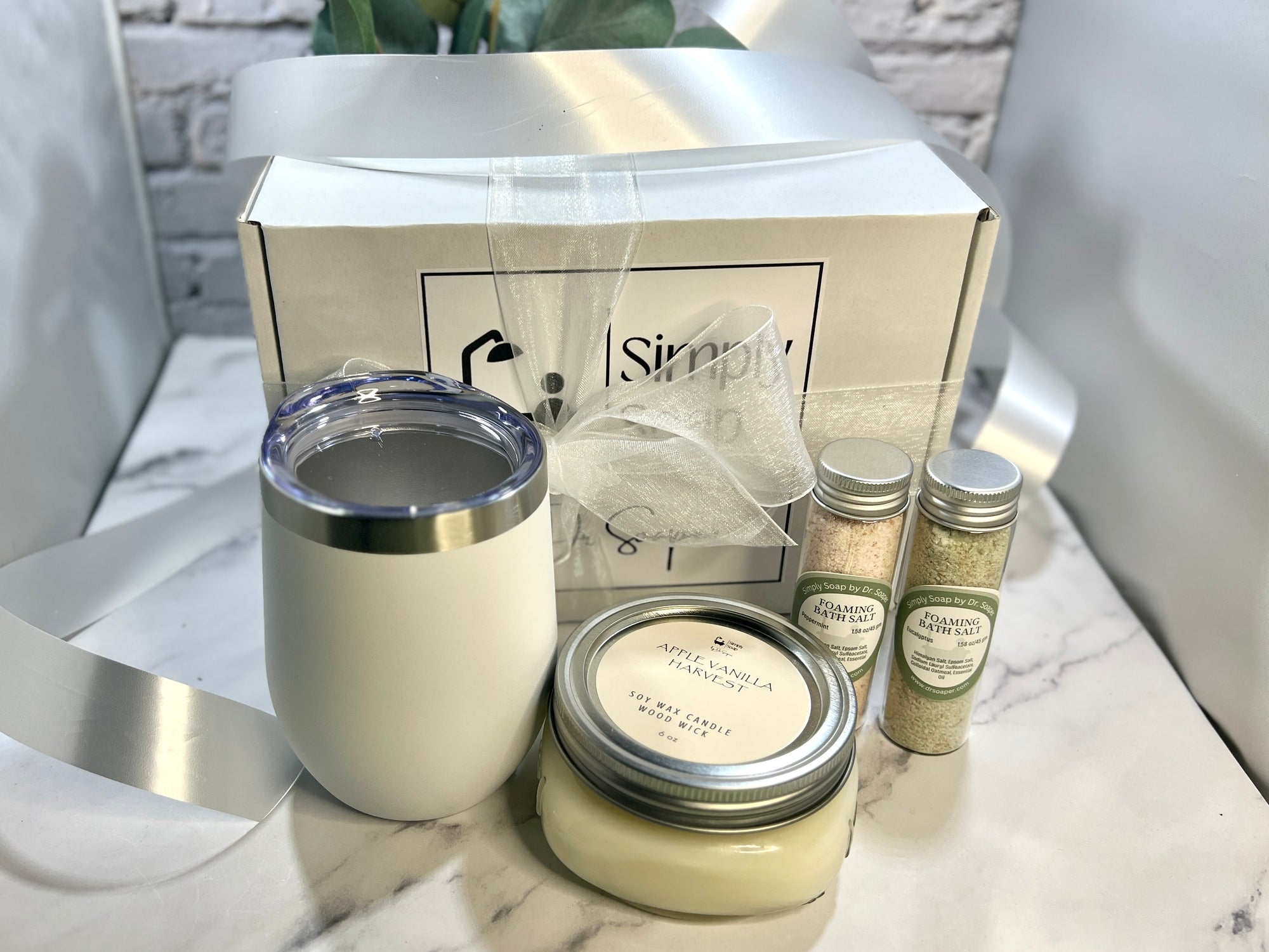 White tumbler, jar, and small bottles with packaging on a marble surface