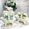 Two small bathtubs with goat milk soaps wrapped in colorful paper on a marble surface.