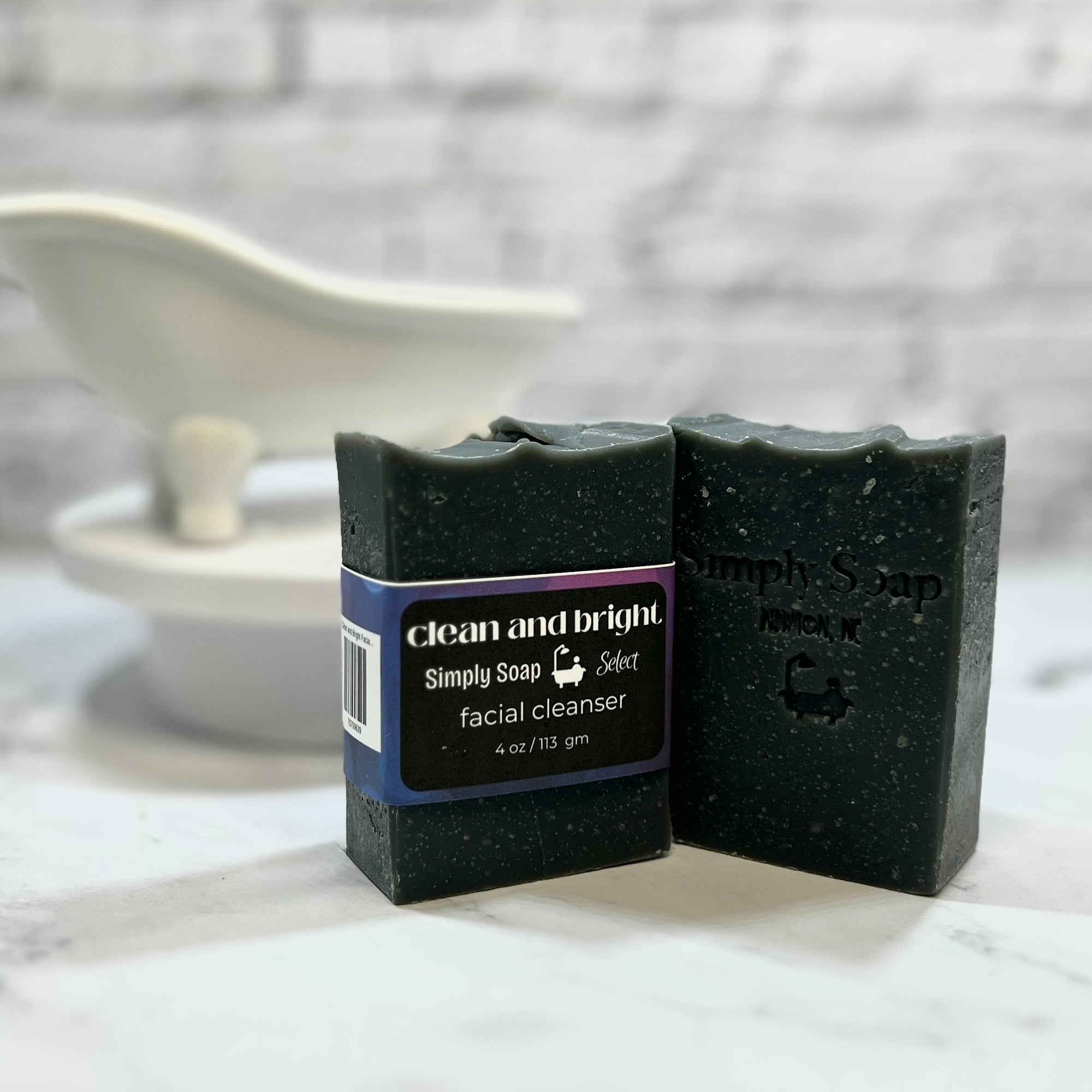 Two bars of black soap with packaging on a marble surface.