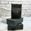 Stack of black soap bars with a label on a white surface and brick wall background