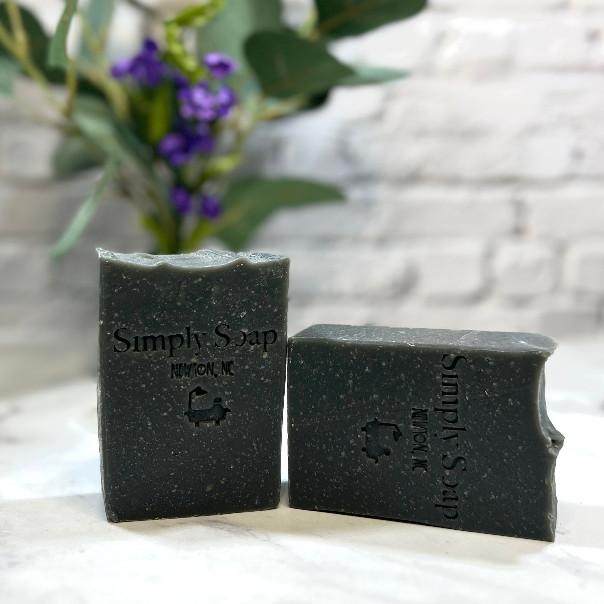 Two bars of 'Simply Soap' on a white surface with a blurred background