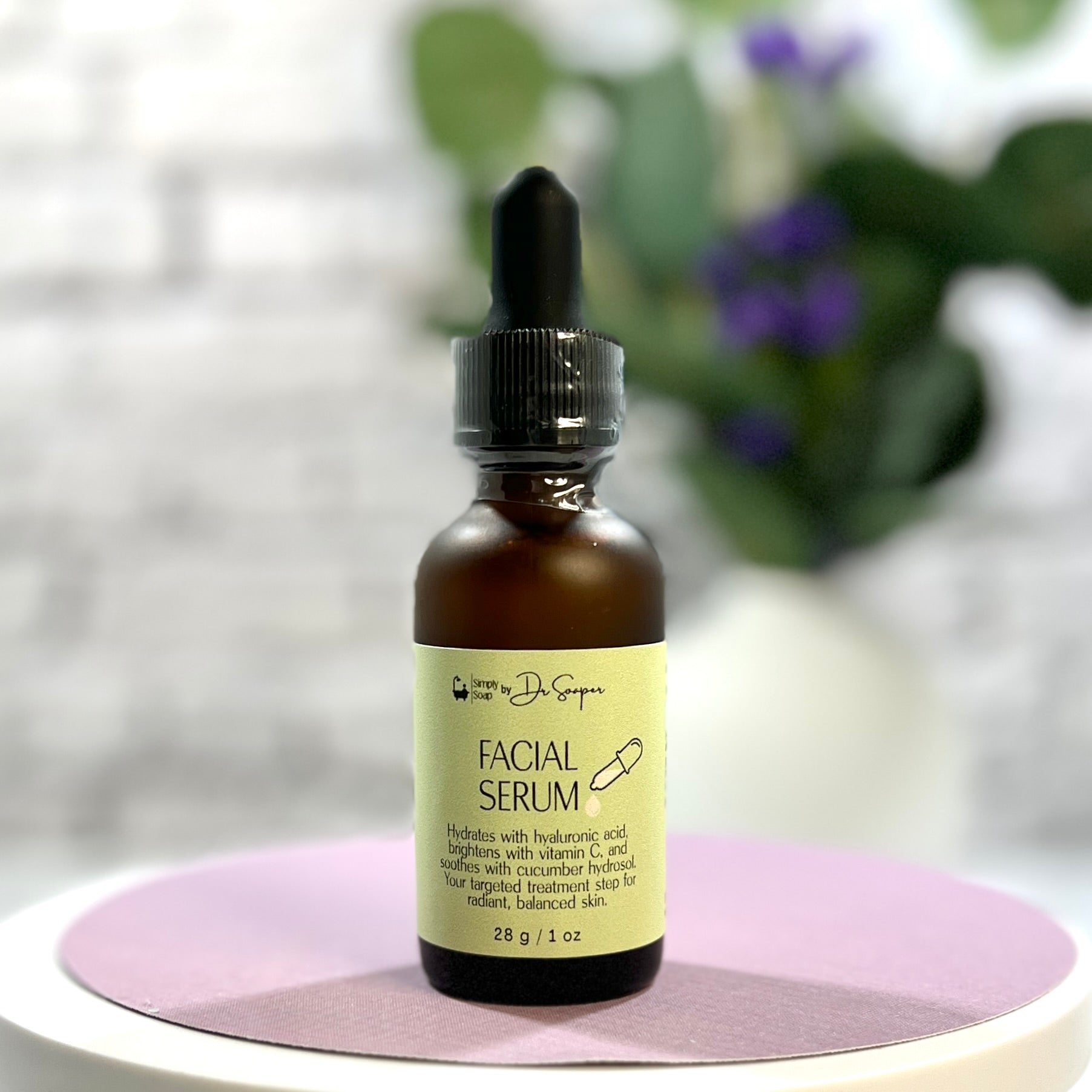 Facial serum bottle with dropper on a white  and lavender surface with blurred greenery in the background