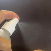 Hand holding a white spray bottle against a dark background