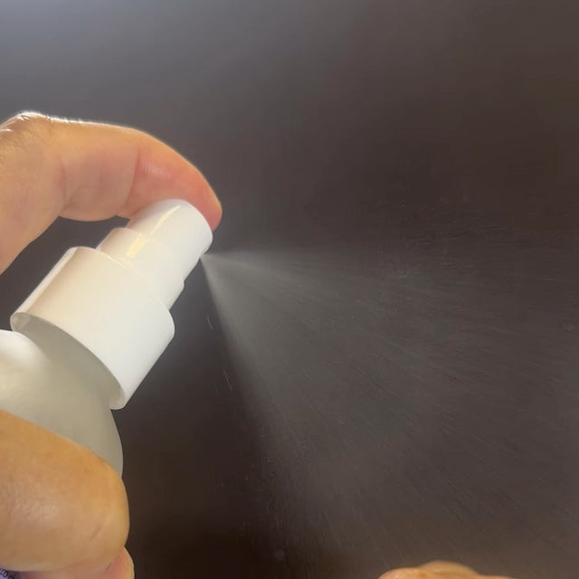 Hand holding a white spray bottle against a dark background