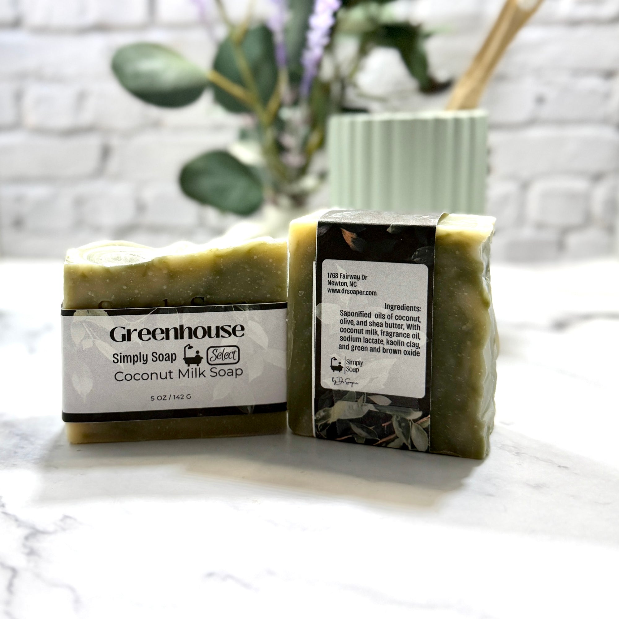 Two bars of Greenhouse coconut milk soap on a marble surface with a blurred plant in the background.