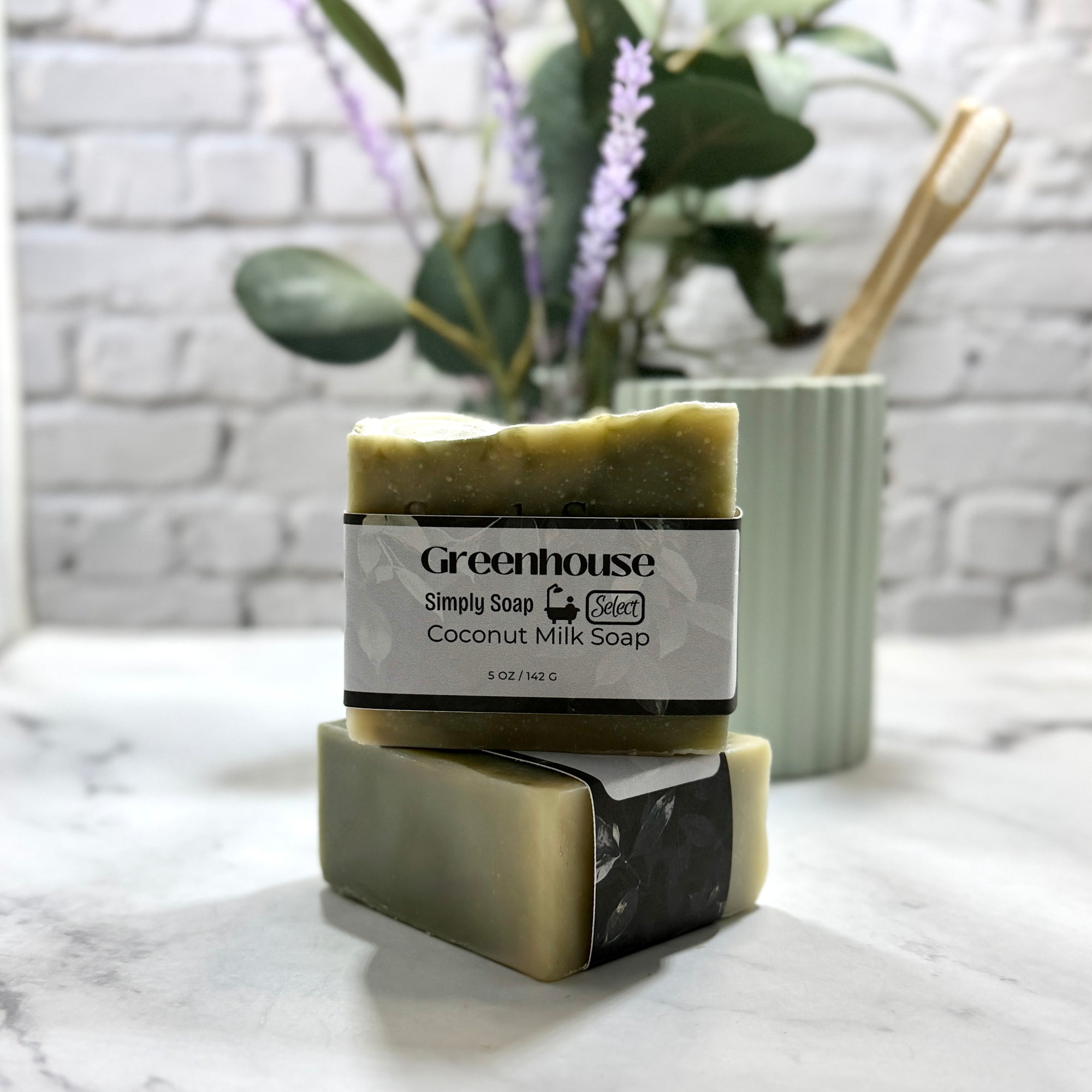 Two bars of Greenhouse coconut milk soap stacked on a marble surface with a plant in the background.