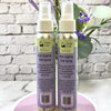 Two bottles of Simply Soap Hair Styling Salt Spray on a white surface with a light gray brick wall background.