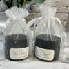 Two black containers of hand cream in clear gift bags with labels on a marble surface.