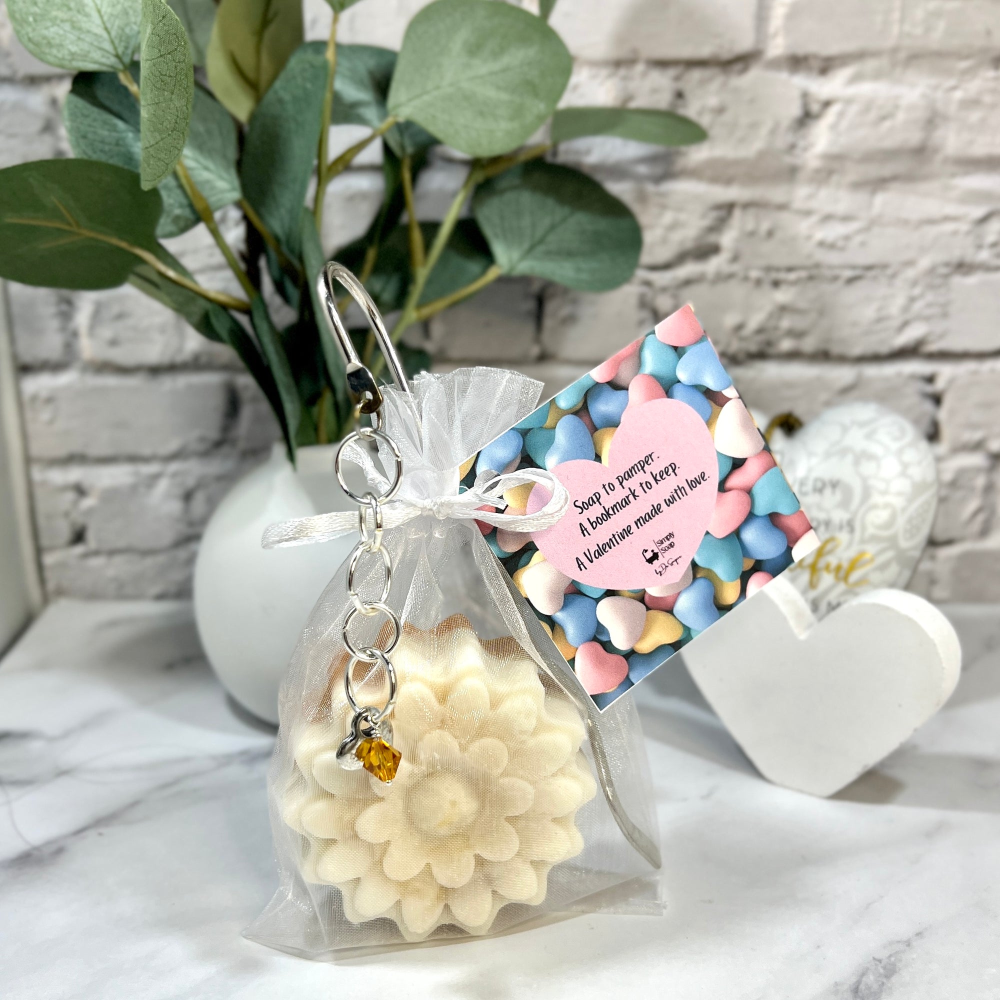 Gift bag with white flowers, decorative tag, and small plant on marble surface