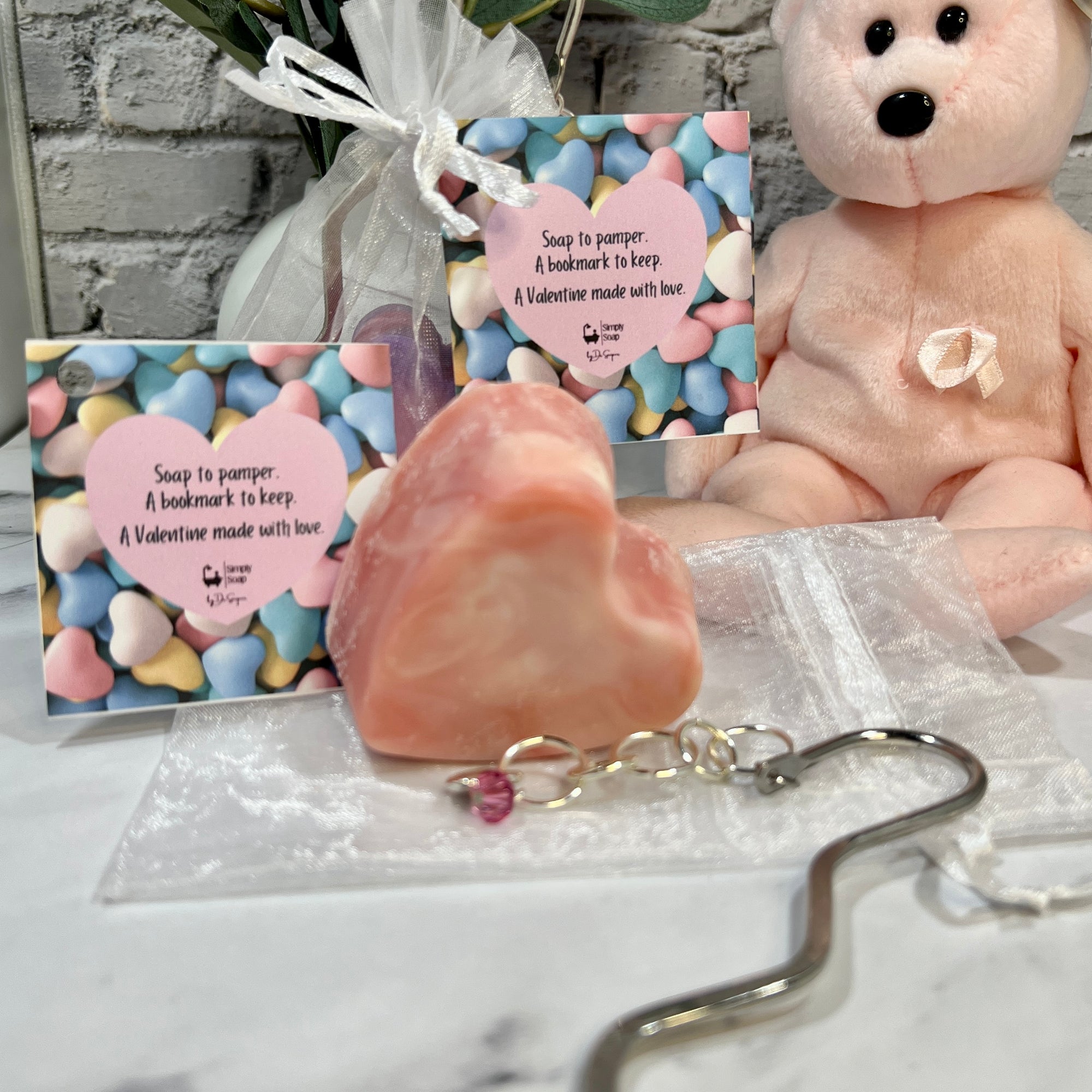 Pink soap with a keychain, teddy bear, and Valentine's Day card on a marble surface.