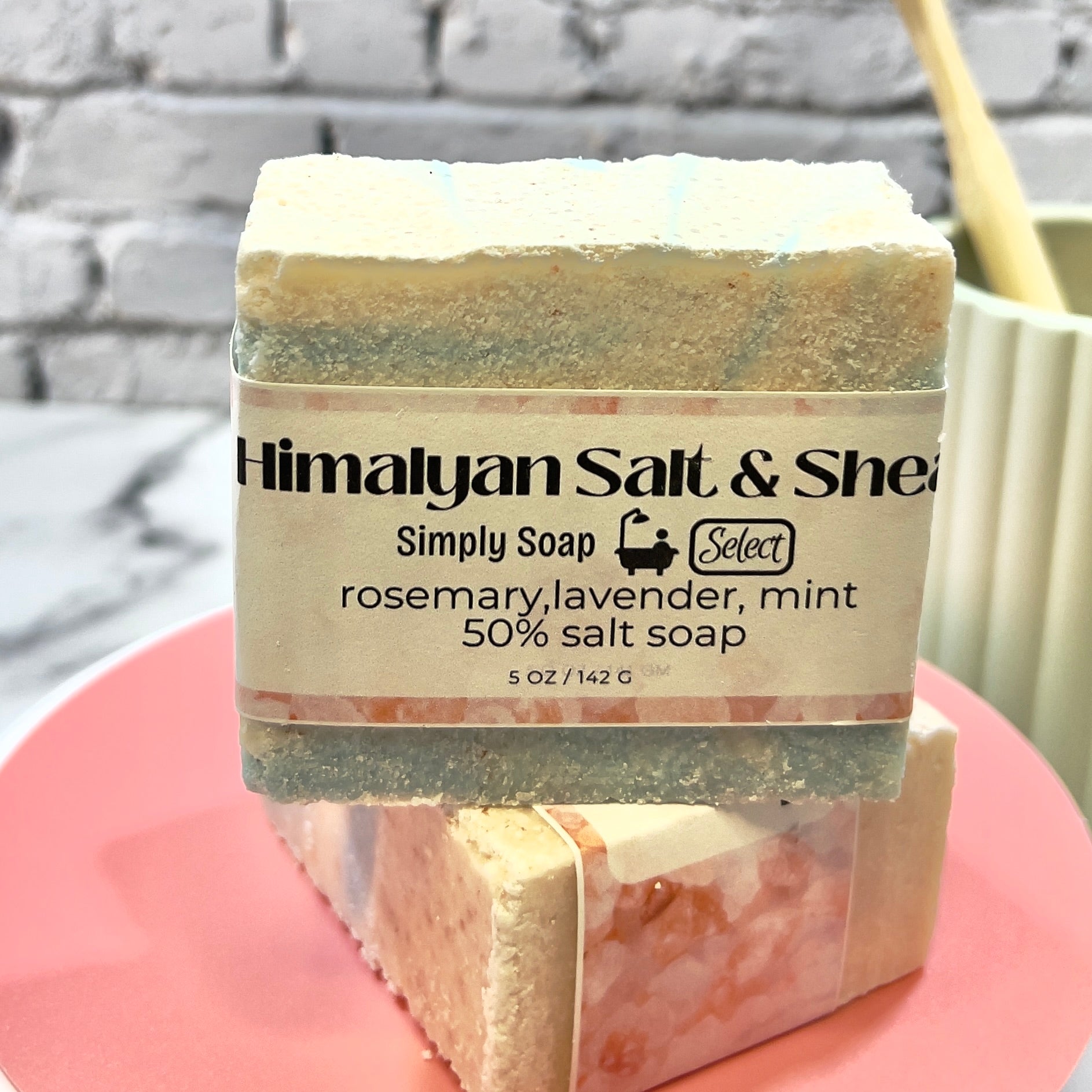 Bar of salt oap with a label on a pink stand against a gray brick wall.