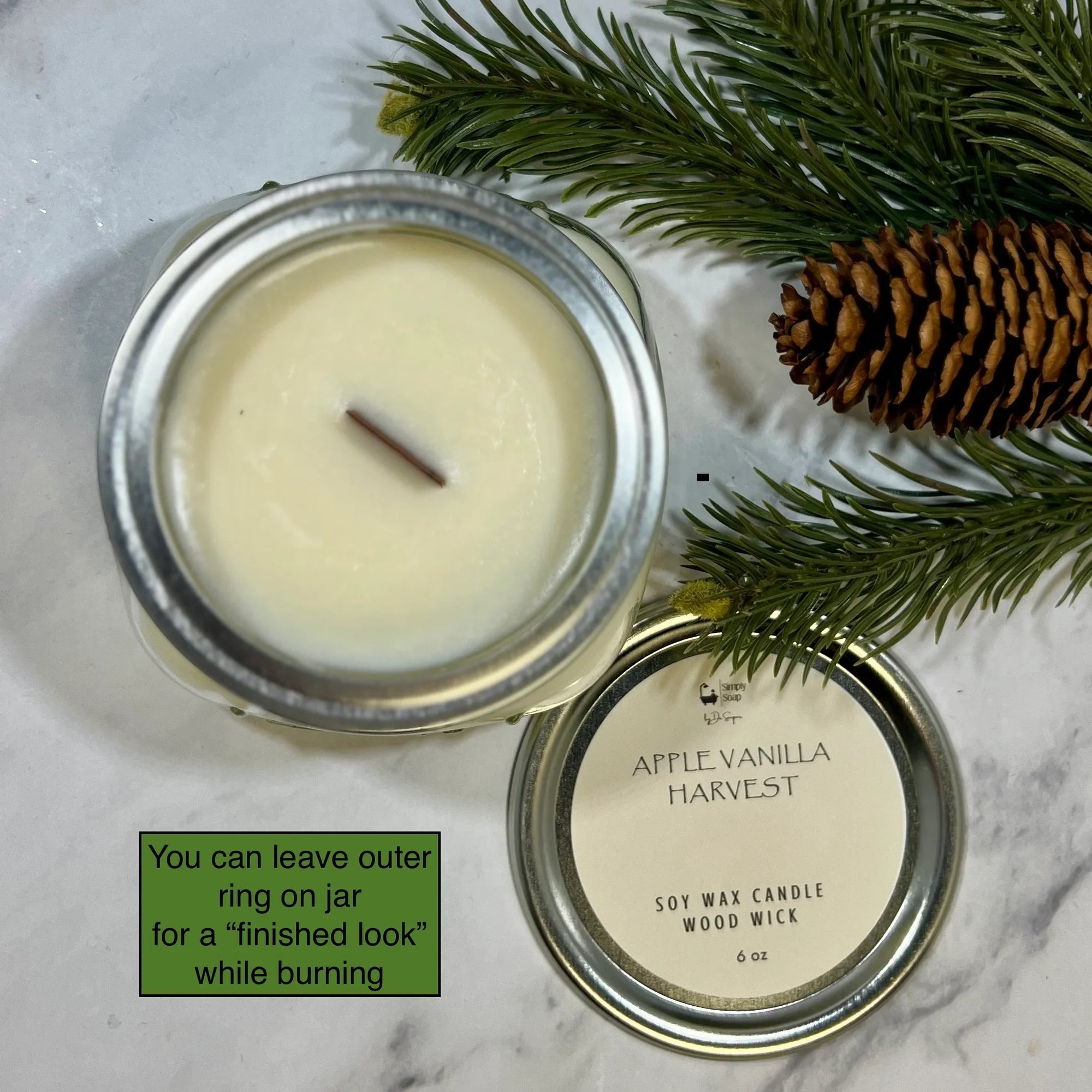 Apple vanilla harvest soy wax candle with metal lid on a marble surface with pine branches and a pine cone.