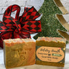Two bars of soap with labels in front of a decorative Christmas tree and gift bag.