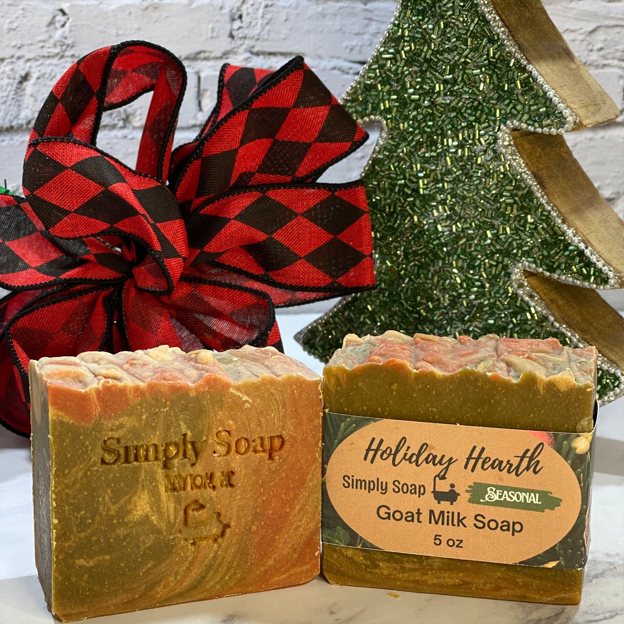 Two bars of soap with labels in front of a decorative Christmas tree and gift bag.