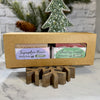 A kraft paper gift box containing two Simply Soap seasonal bars: displayed on a wooden snowflake stand.