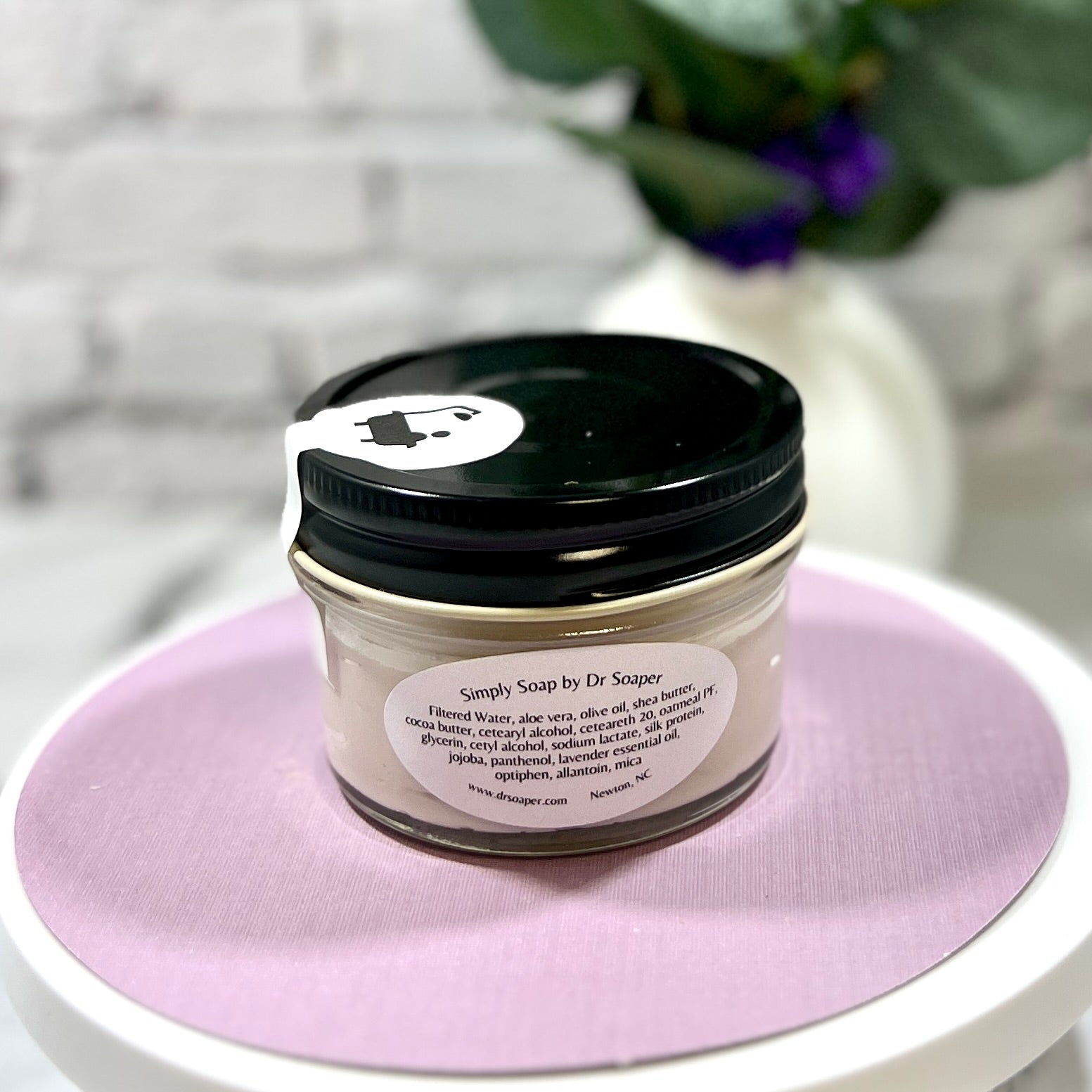 Back of Jar of hand cream on a pink surface with a blurred background