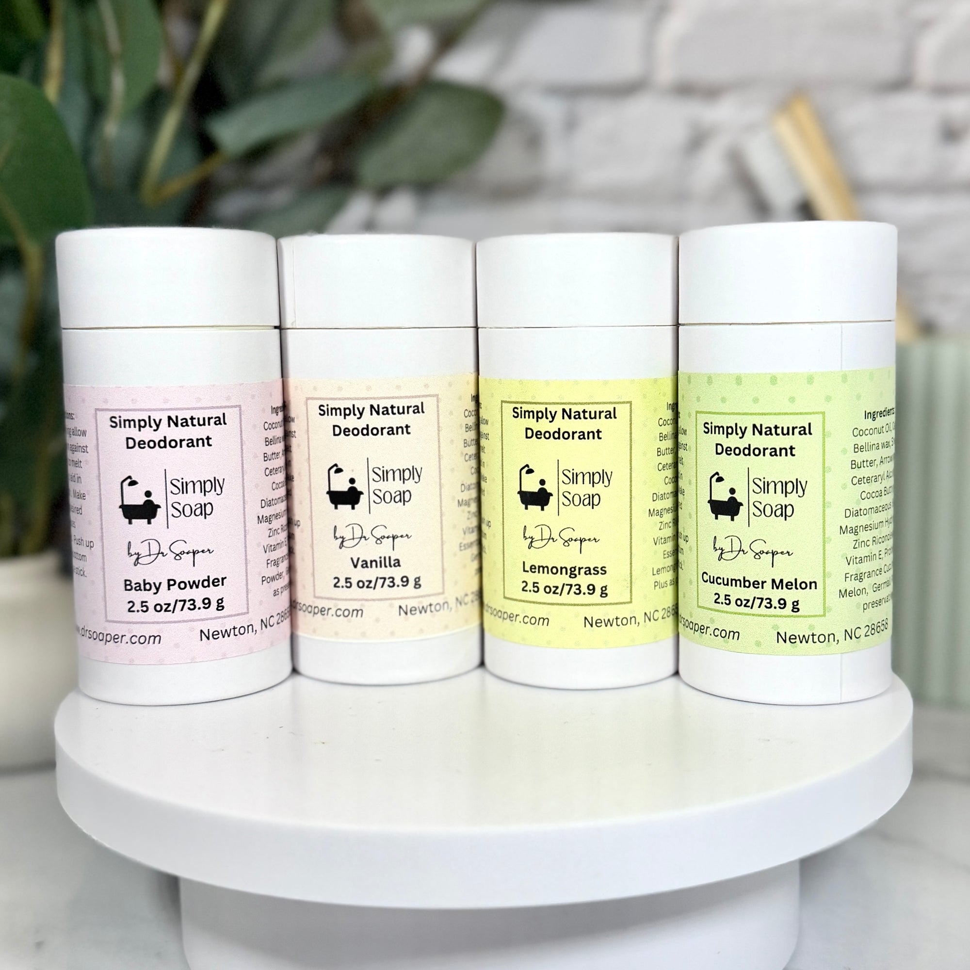 FourSimply Natural Deodorant containers on a white stand with a blurred background