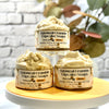 Three Oatmeal Crumble Cupcake Soaps on a white stand with a blurred plant background