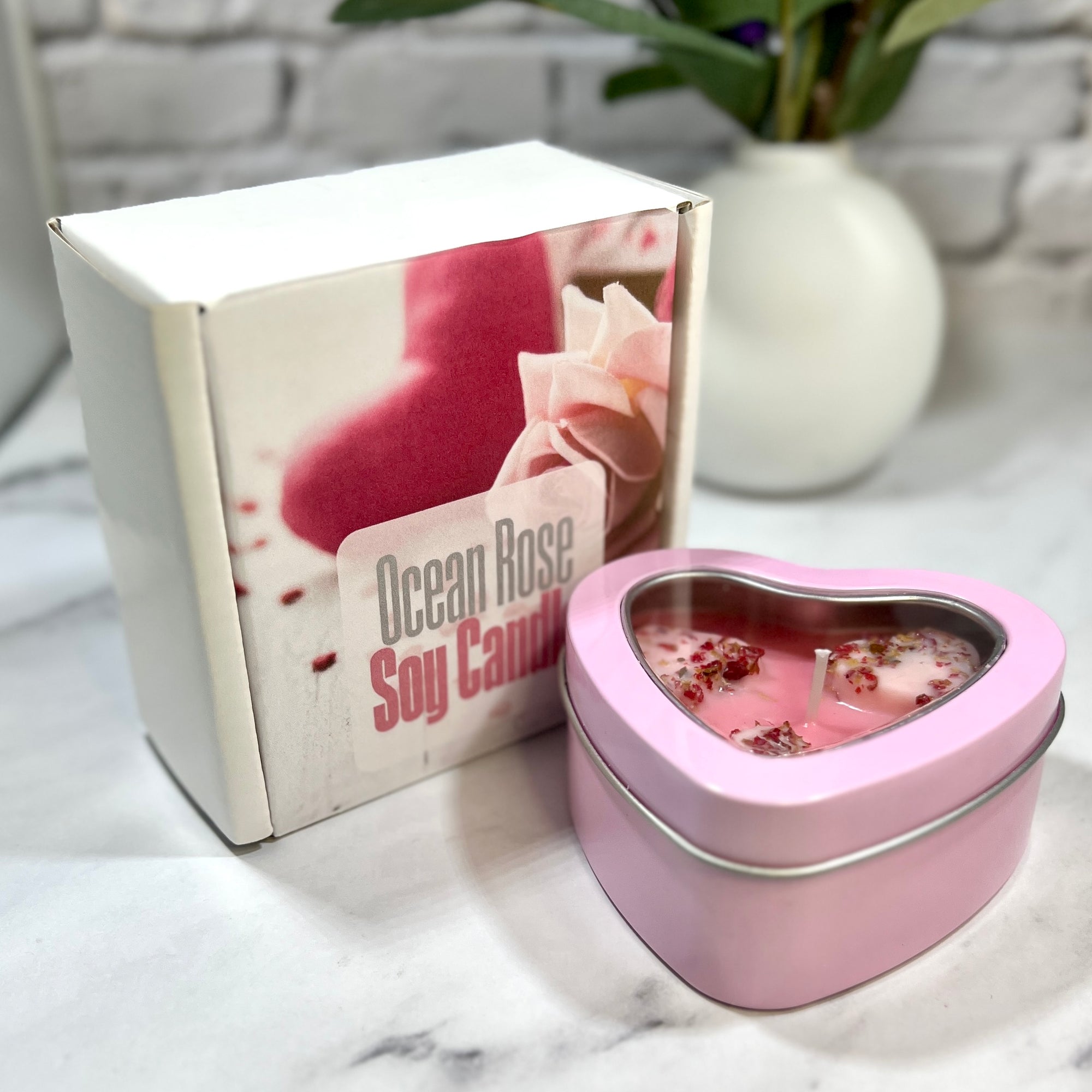 Heart-shaped pink candle in a tin with 'Ocean Rose Soy Candle' packaging on a marble surface.