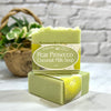 Two bars of Pear Prosecco Coconut Milk Soap on a marble surface with a basket of flowers in the background.