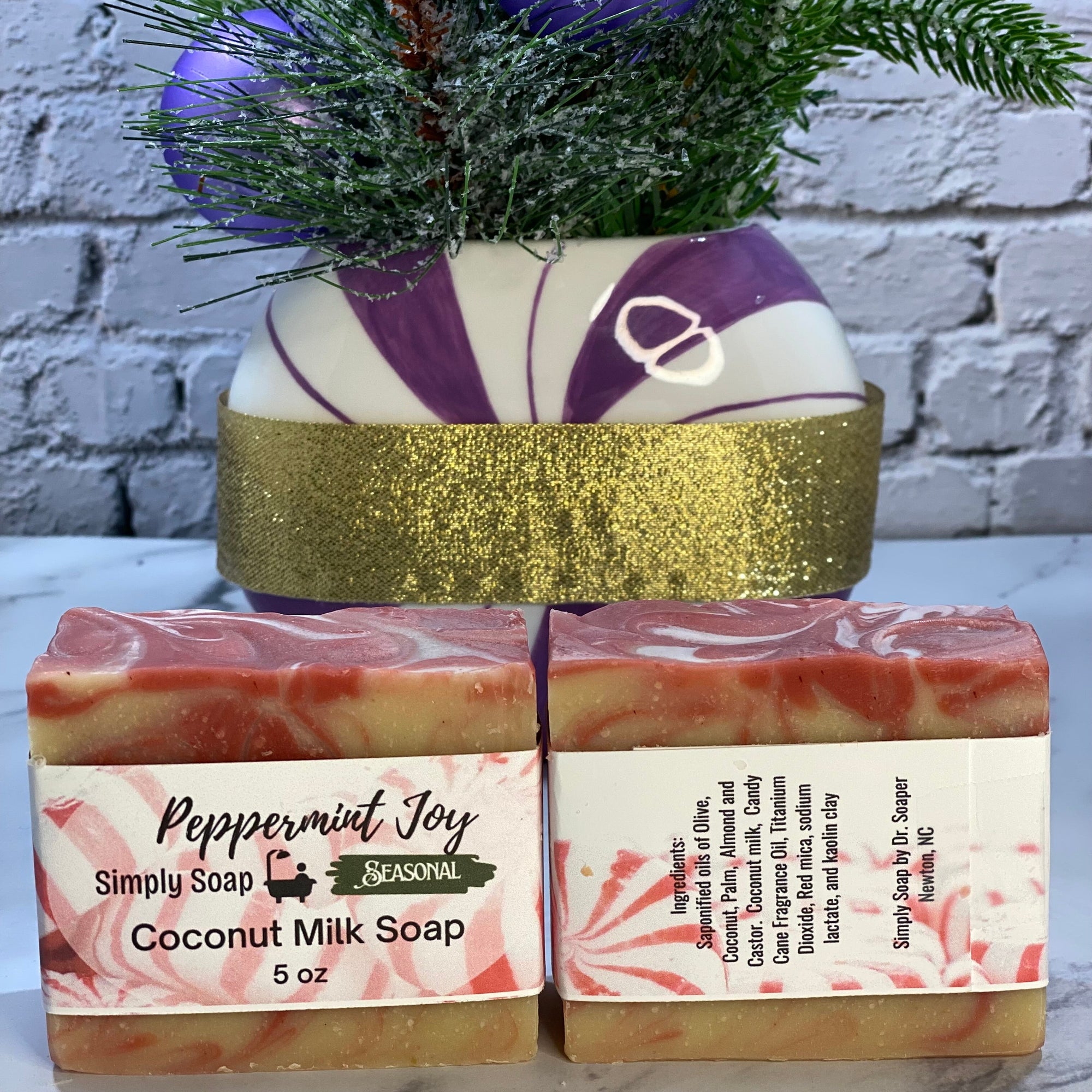 Two bars of coconut milk  peppermint soap with a decorative soap and plant on a marble surface.