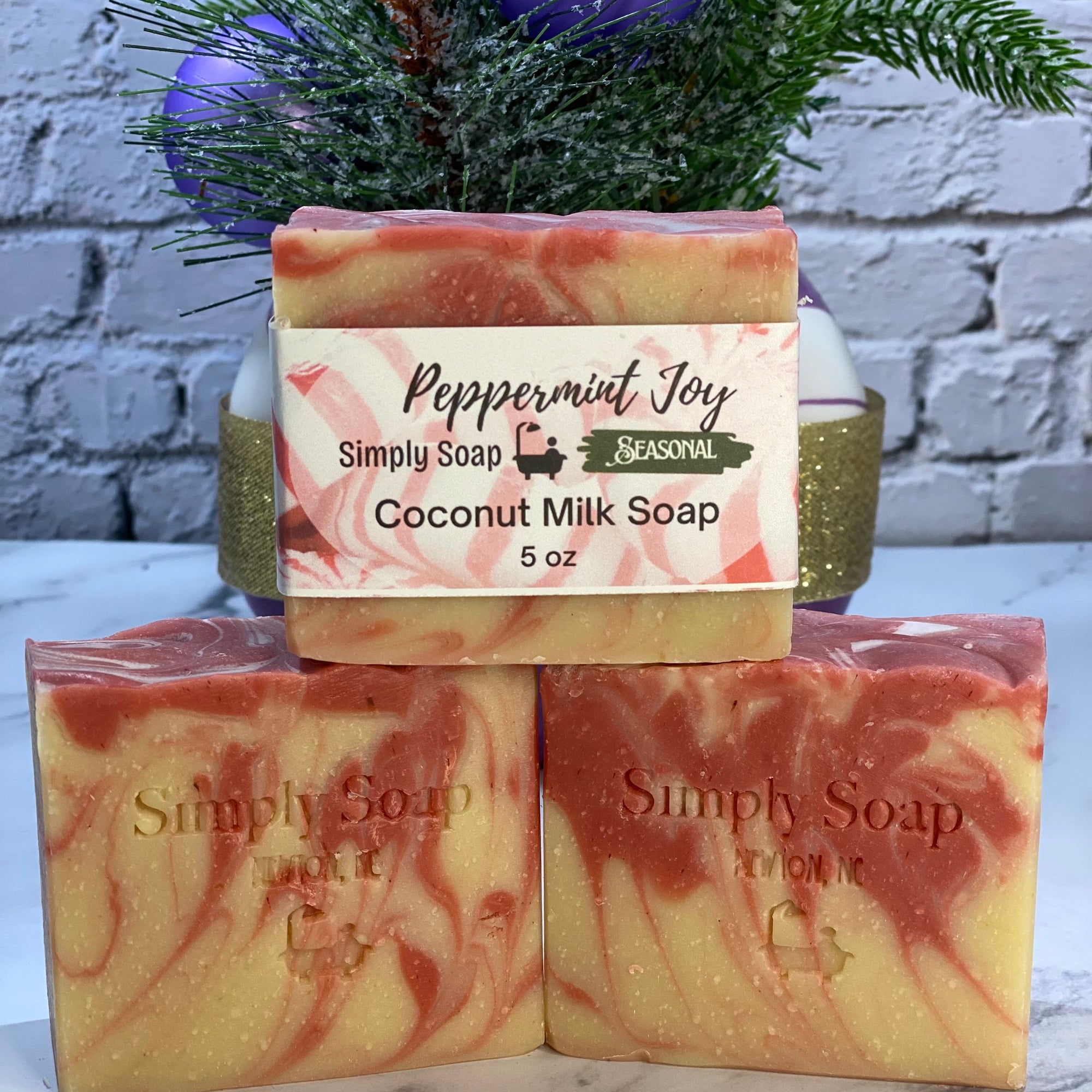 Three bars of soap with a decorative plant and purple ornament in the background.