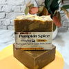 Pumpkin Spice goat milk soap bar with packaging on a yellow stand against a blurred background