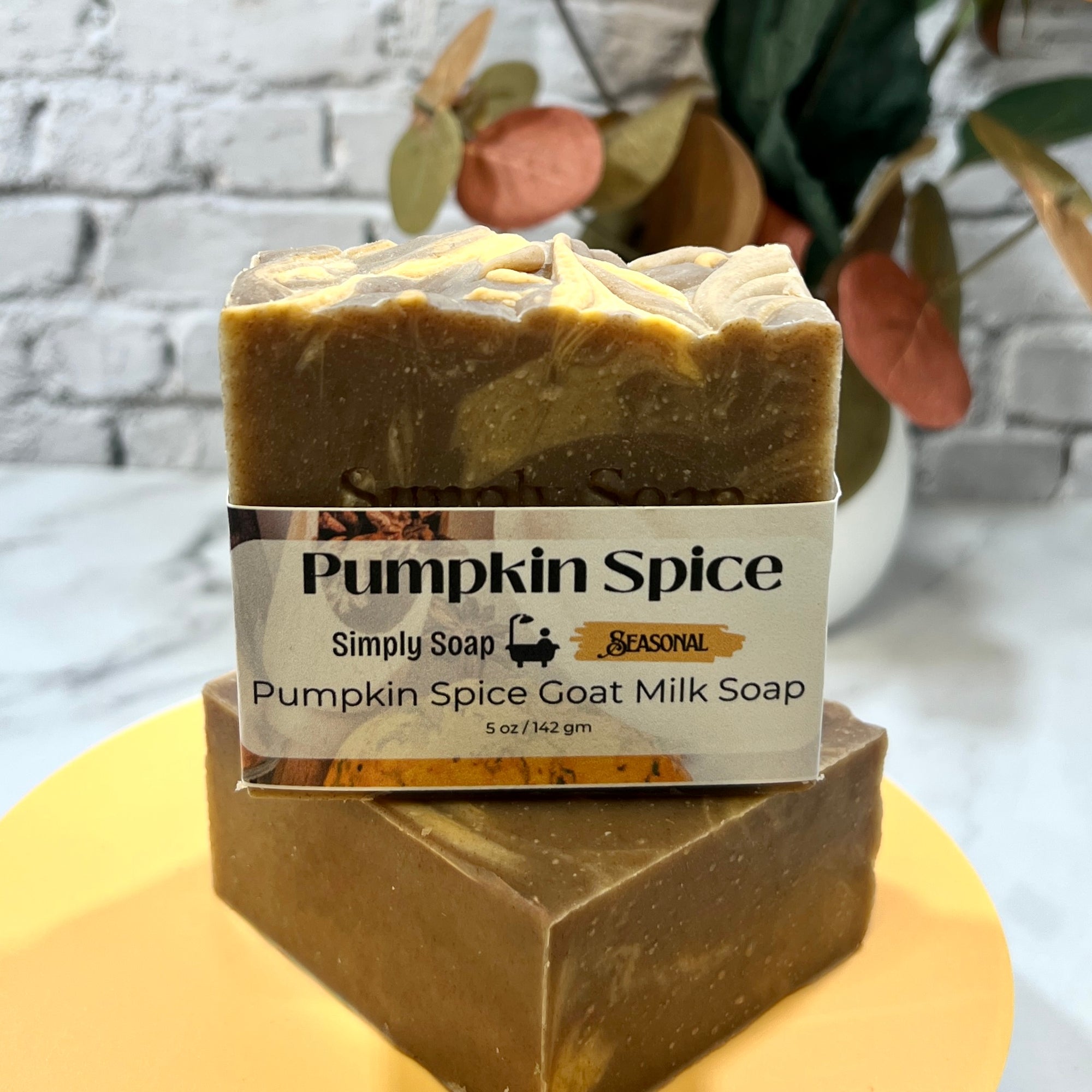 Pumpkin Spice goat milk soap bar with packaging on a yellow stand against a blurred background