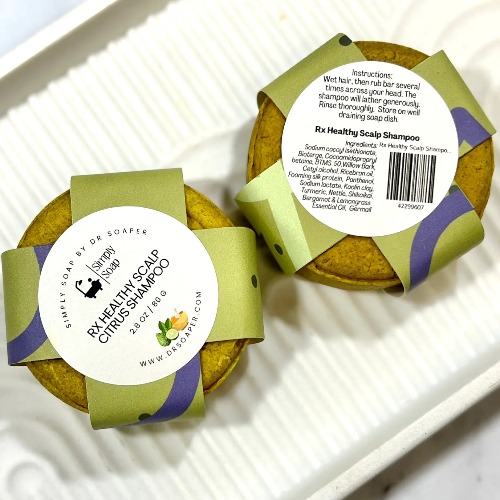 Two round soap bars with green and purple packaging on a white surface