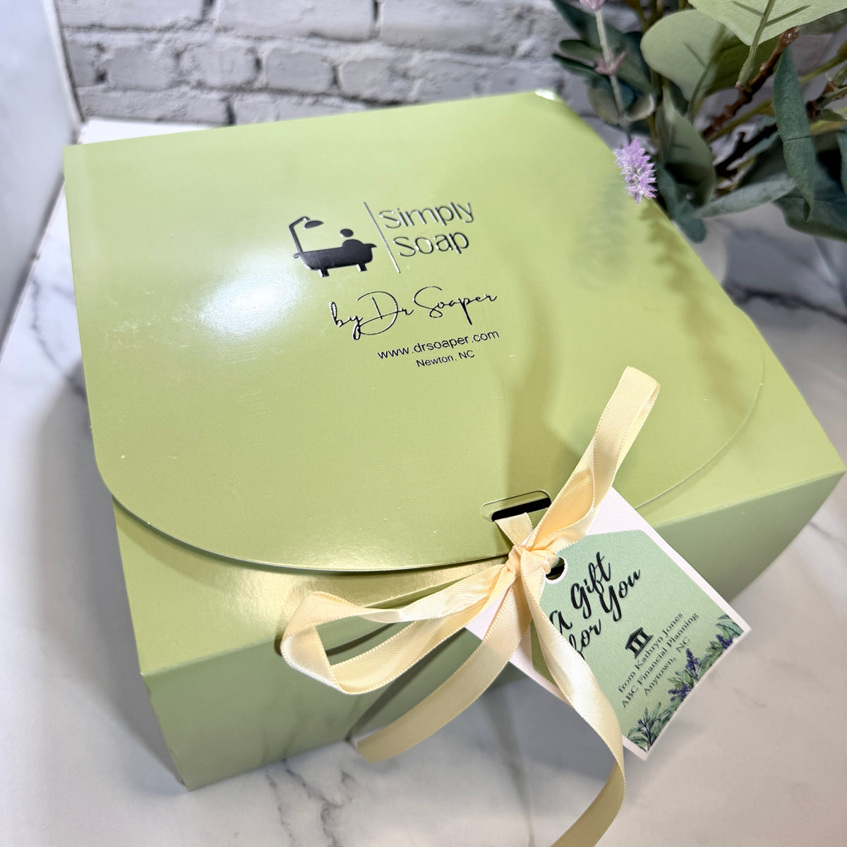 A light green gift box from Simply Soap by Dr Soaper filled with self care items and  tied with a cream ribbon and a 'A Gift for You' tag. 