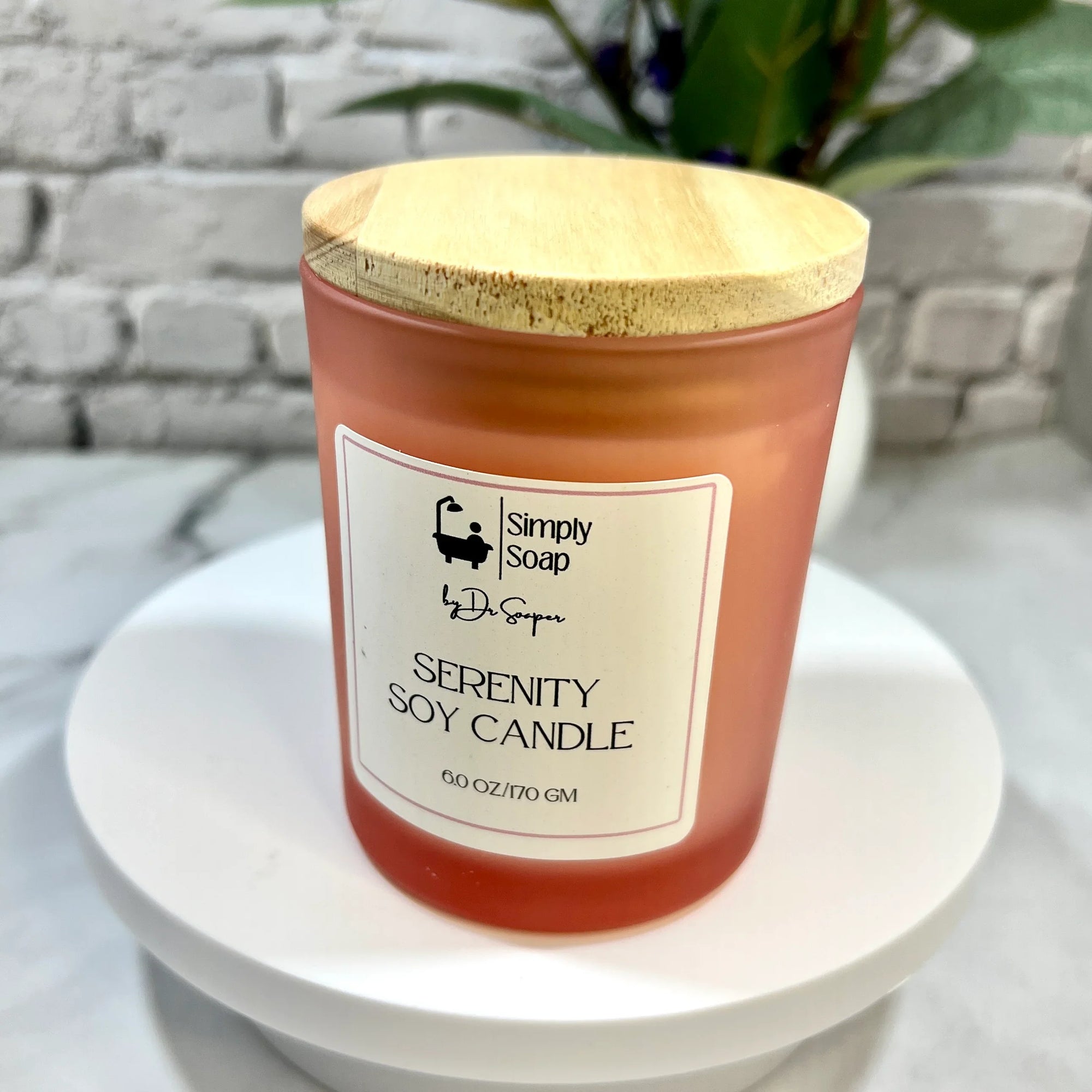 Serenity soy candle with a wooden lid on a white surface, against a gray brick wall.